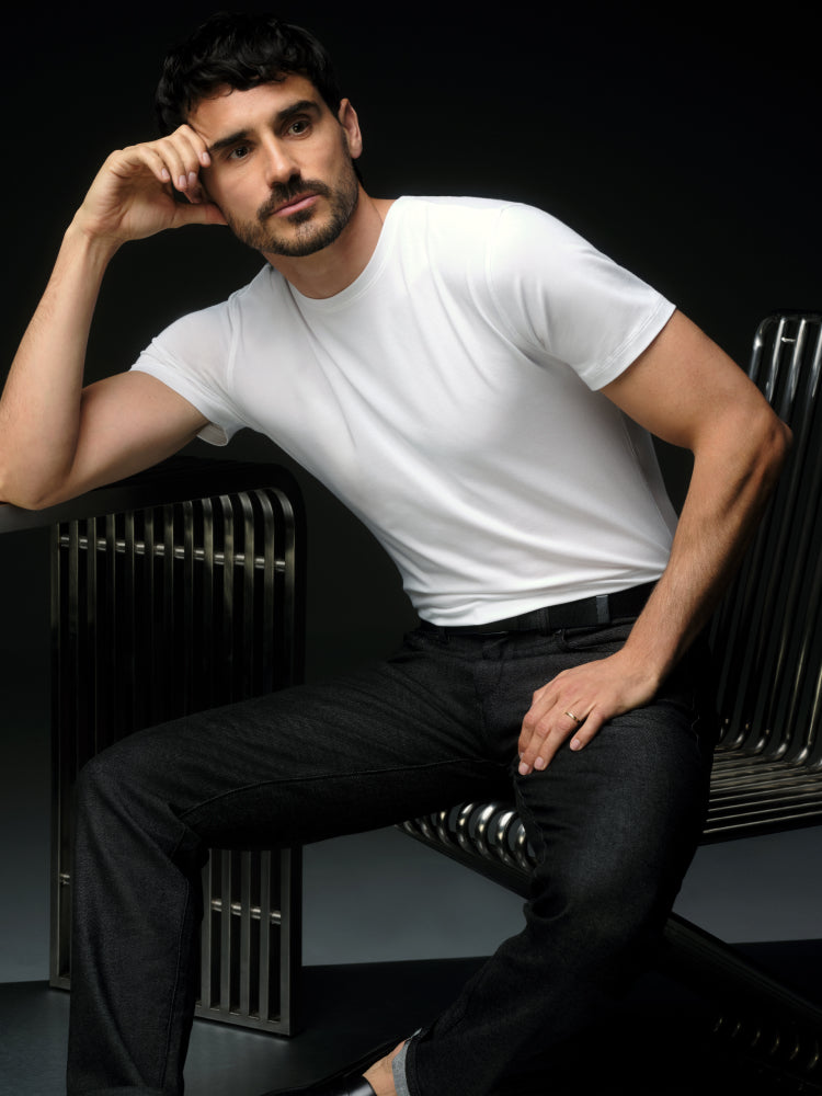 image of a man wearing a white SILVER t-shirt and black SILVER denim pants sitting on a metal chair