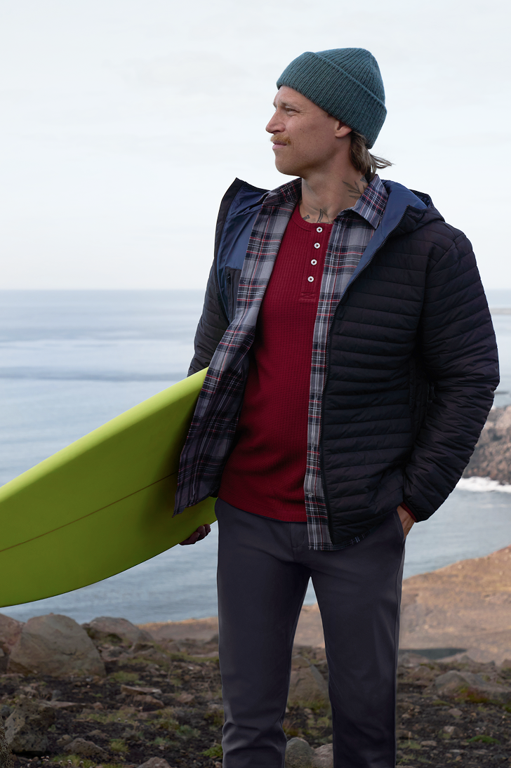 Man holding a surfing board and wearing WARMKNIT AIR Hooded Jacket