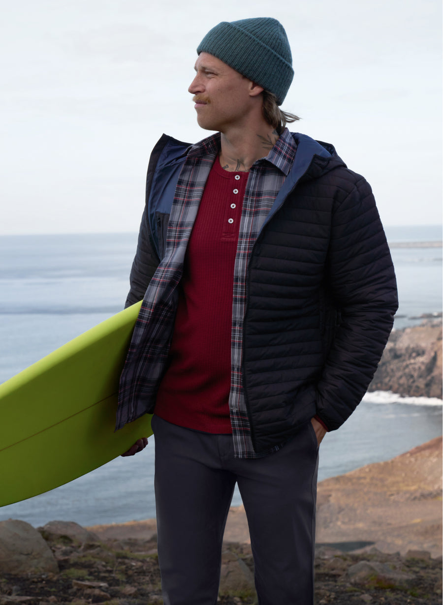 Man carrying a surfboard and wearing Warmknit air hooded jacket