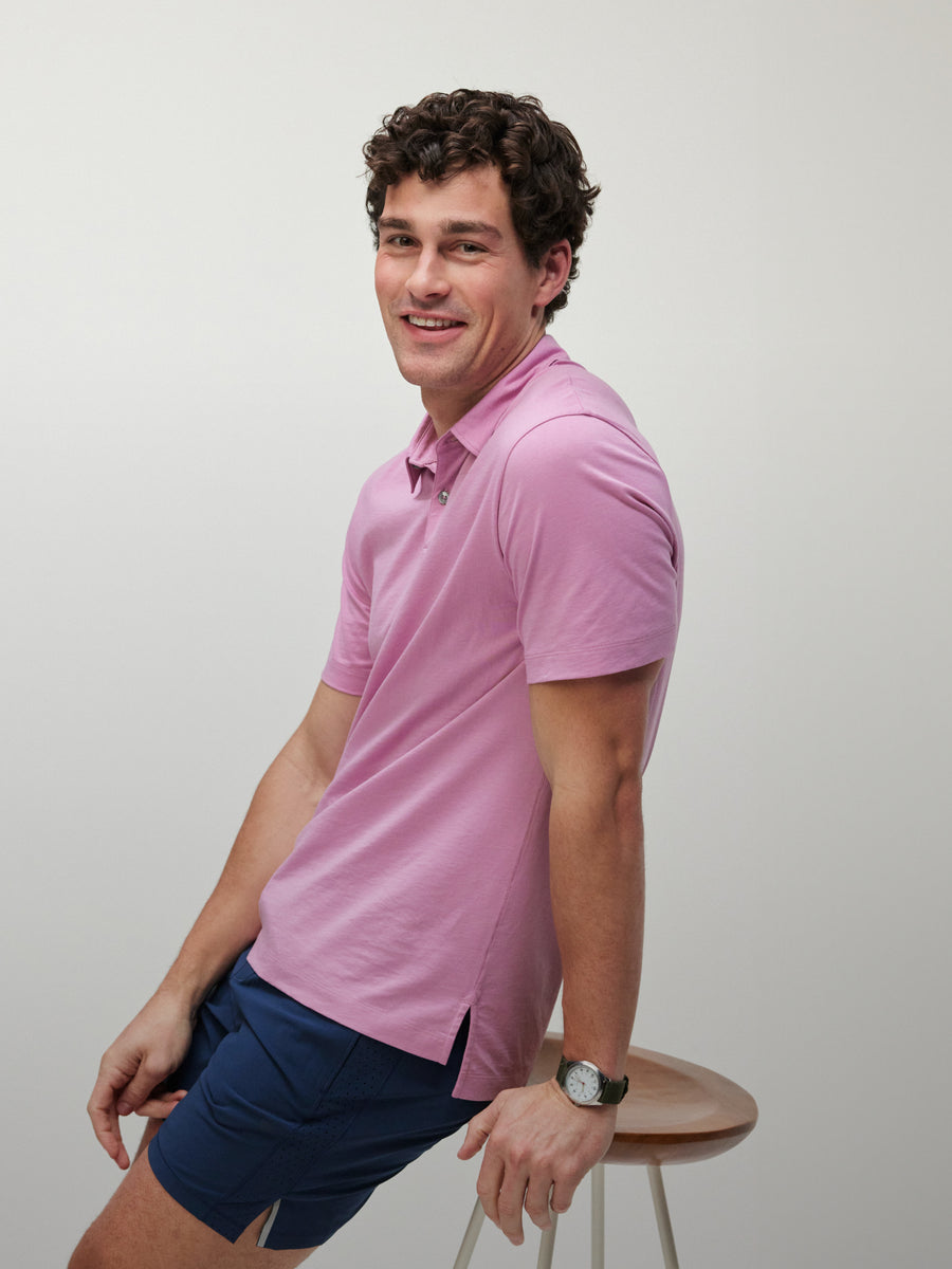 Man sits on a stool wearing a pink polo and navy shorts