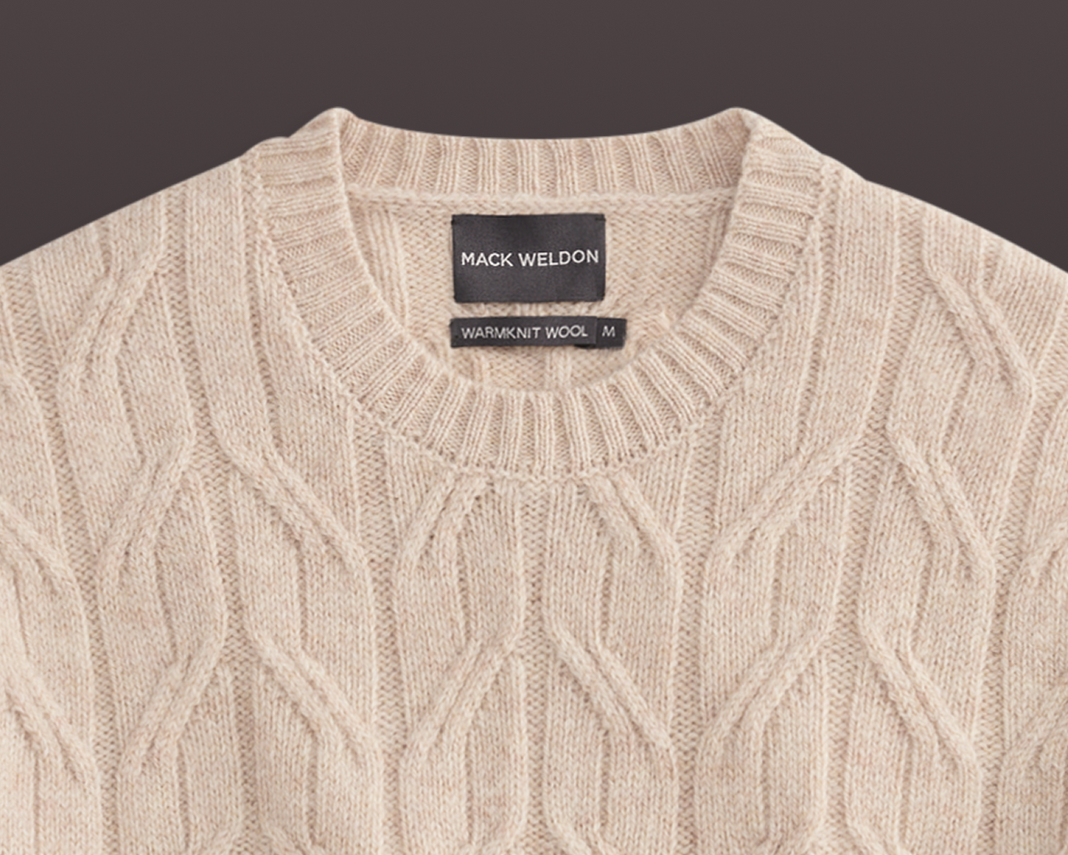 Beige cable knit sweater with Mack Weldon label on a dark background