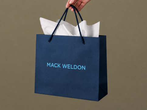 Navy blue paper shopping bag with black handles and the brand name 'MACK WELDON' 